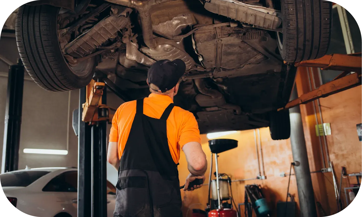 A man is working under a car on a lift in a garage.