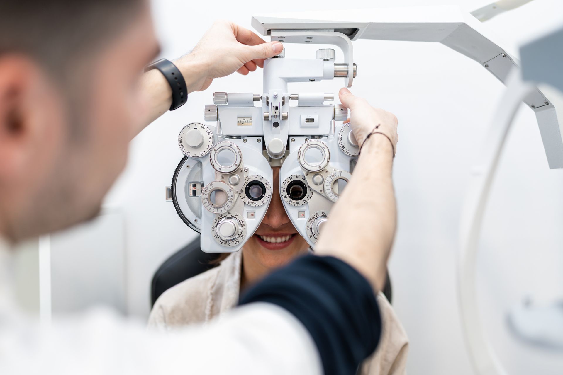 An Optometrist conducts a phoropter eye test for a young woman in an optical shop.