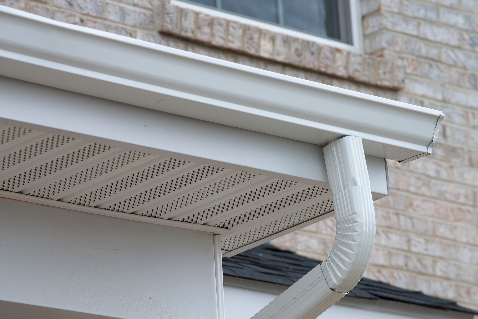 A white gutter on the side of a brick house.