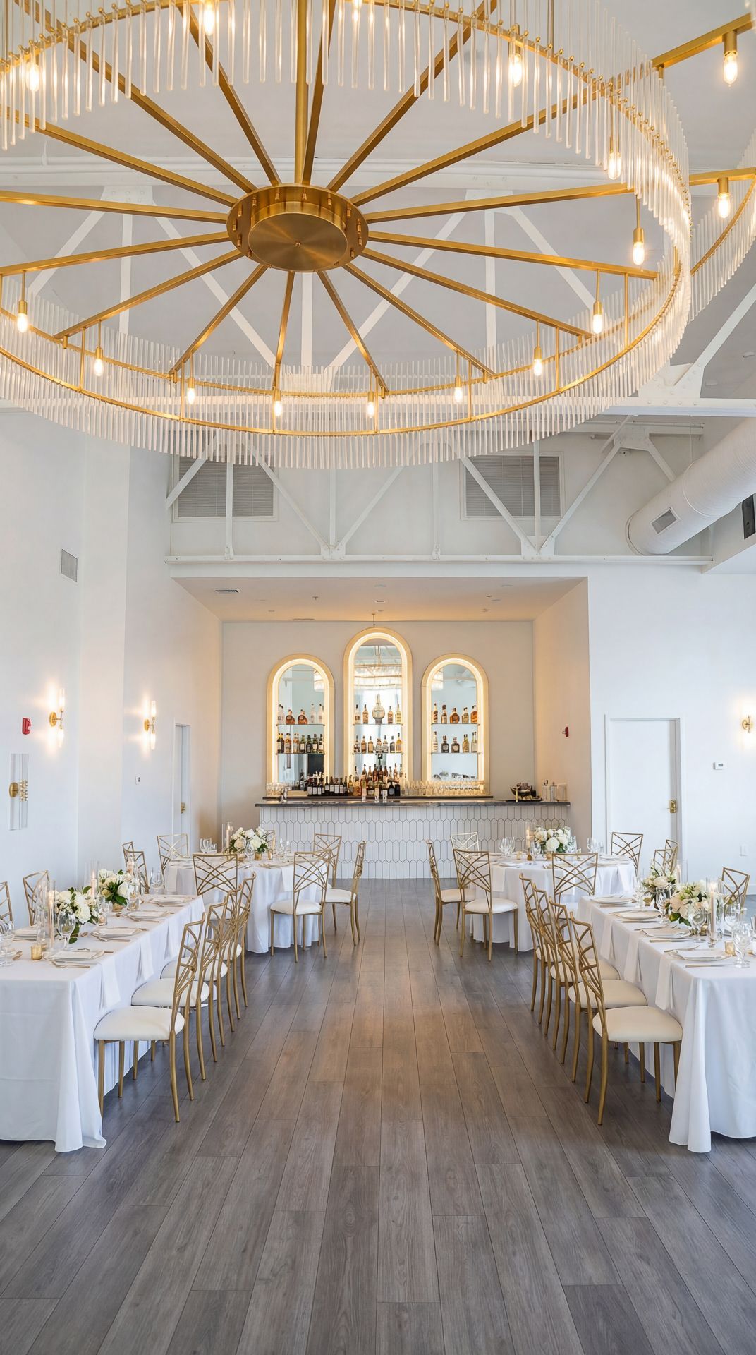 Elegant wedding reception hall with round and rectangular tables, gold accents, and a large chandelier.