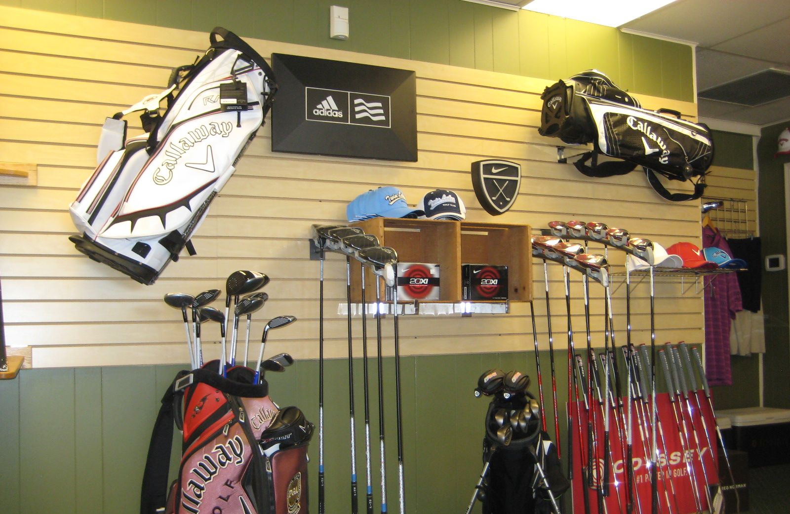 Golf equipment display in a store, including golf bags, clubs, and hats on a slatted wall.