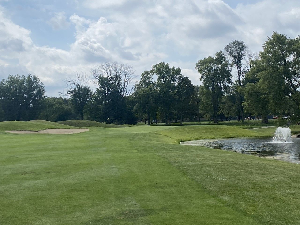 Green golf course with a pond, trees, and cloudy sky.