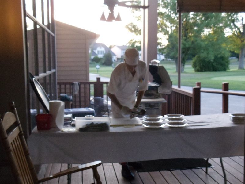 Chef preparing food on a table outdoors; plates and ingredients ready.