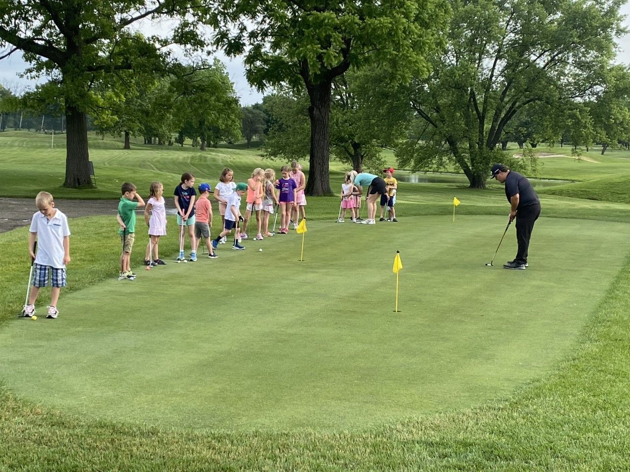 Children watch an instructor putting on a putting green at an outdoor golf course.