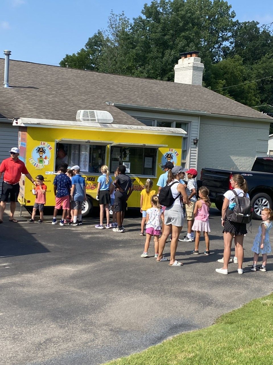 People line up at a yellow food truck in front of a building.