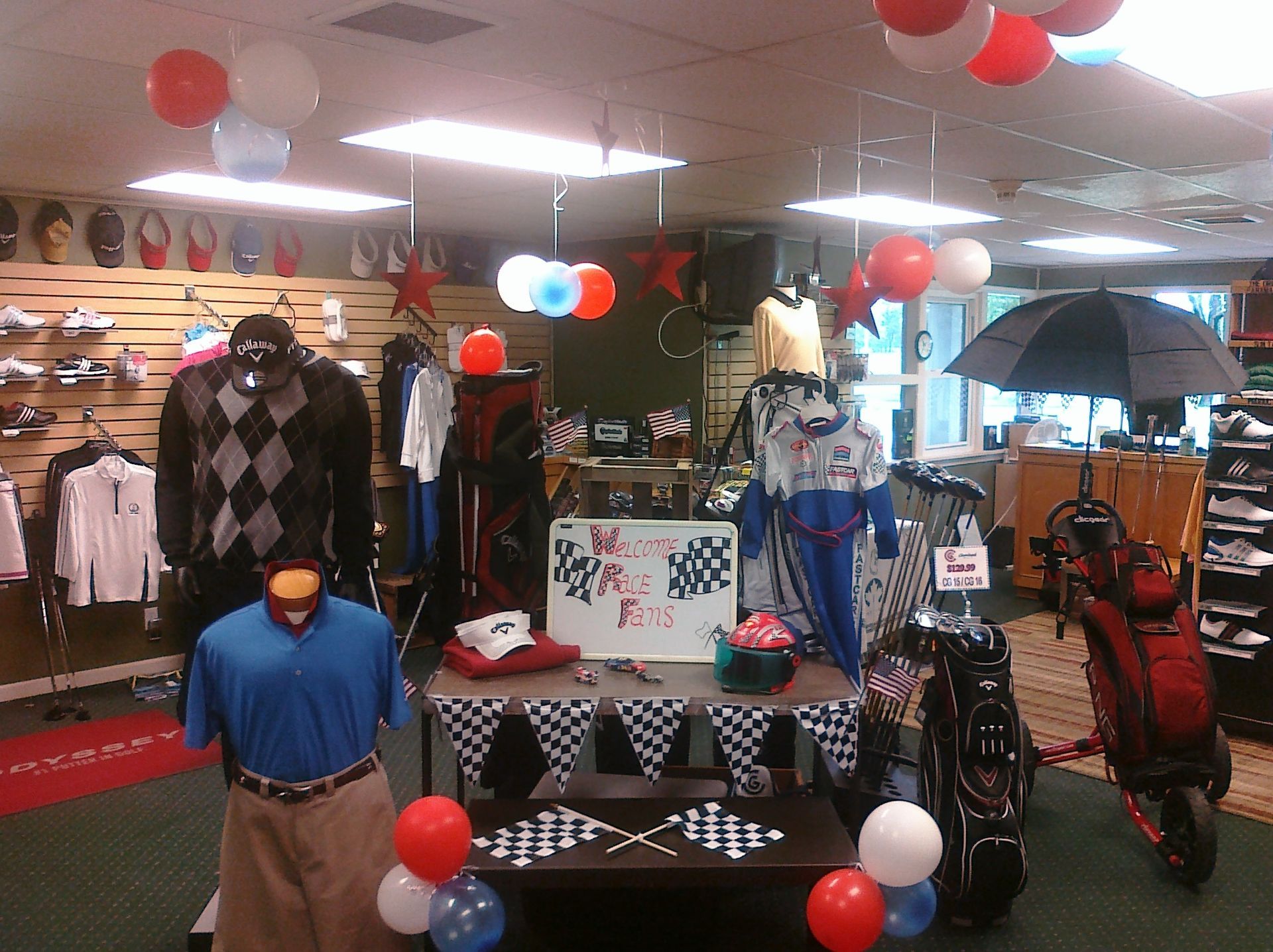 Golf store interior with clothing, shoes, and equipment displayed. Decorated with balloons and checkered flag for an event.