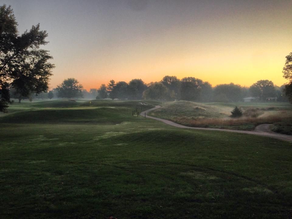 Golf course at sunrise, with trees and a winding path, bathed in golden light.
