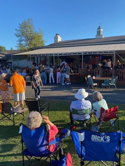 Golfers practicing swings on a green course, with a golf bag in foreground, and trees in the background.