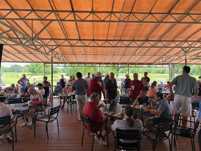 Two women smiling in a golf shop. They wear blue golf shirts, posing near colorful shirts on display.