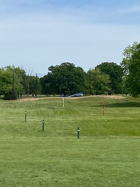Two men in red polo shirts and shorts stand on a golf course.