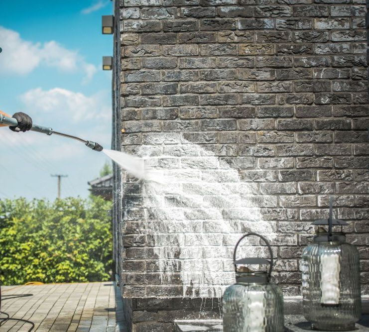 A Person is Using a High Pressure Washer to Clean a Brick Wall — Exquisite Exterior Cleaning In Matcham, NSW