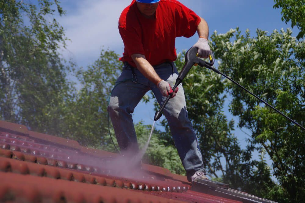 A Man is Cleaning a Roof With a High Pressure Washer — Exquisite Exterior Cleaning In North Gosford, NSW