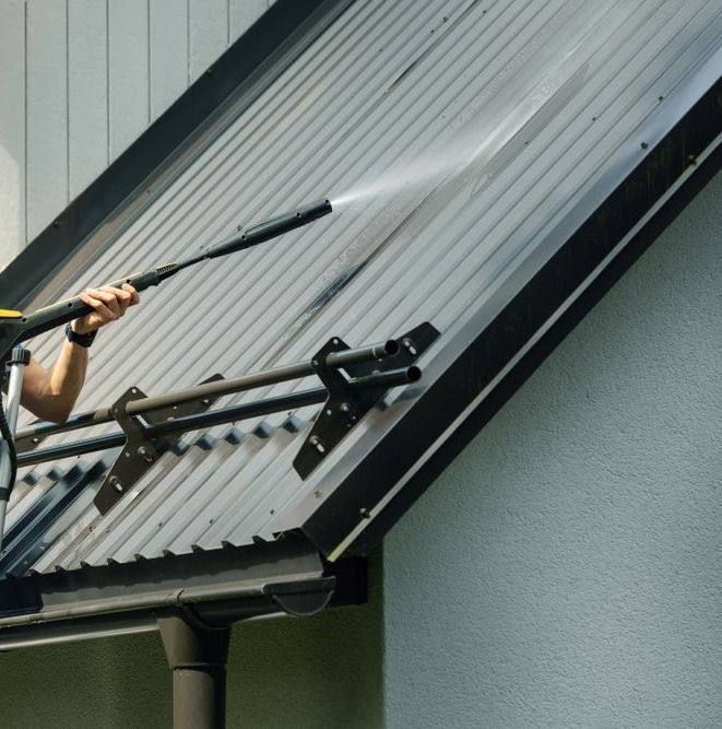 A Man is Cleaning the Roof of a House With a High Pressure Washer — Exquisite Exterior Cleaning In North Gosford, NSW