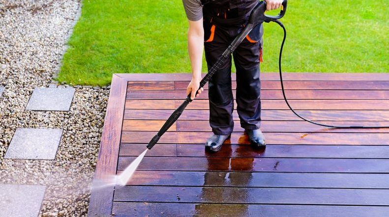 A Man is Using a High Pressure Washer to Clean a Wooden Deck — Exquisite Exterior Cleaning In North Gosford, NSW