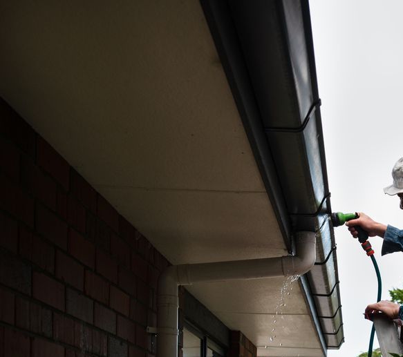 A Man is Spraying a Gutter With a Green Hose — Exquisite Exterior Cleaning In Matcham, NSW