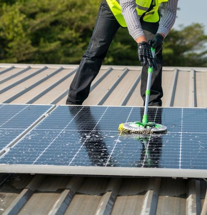 A Man is Cleaning Solar Panels on a Roof With a Mop — Exquisite Exterior Cleaning In North Gosford, NSW