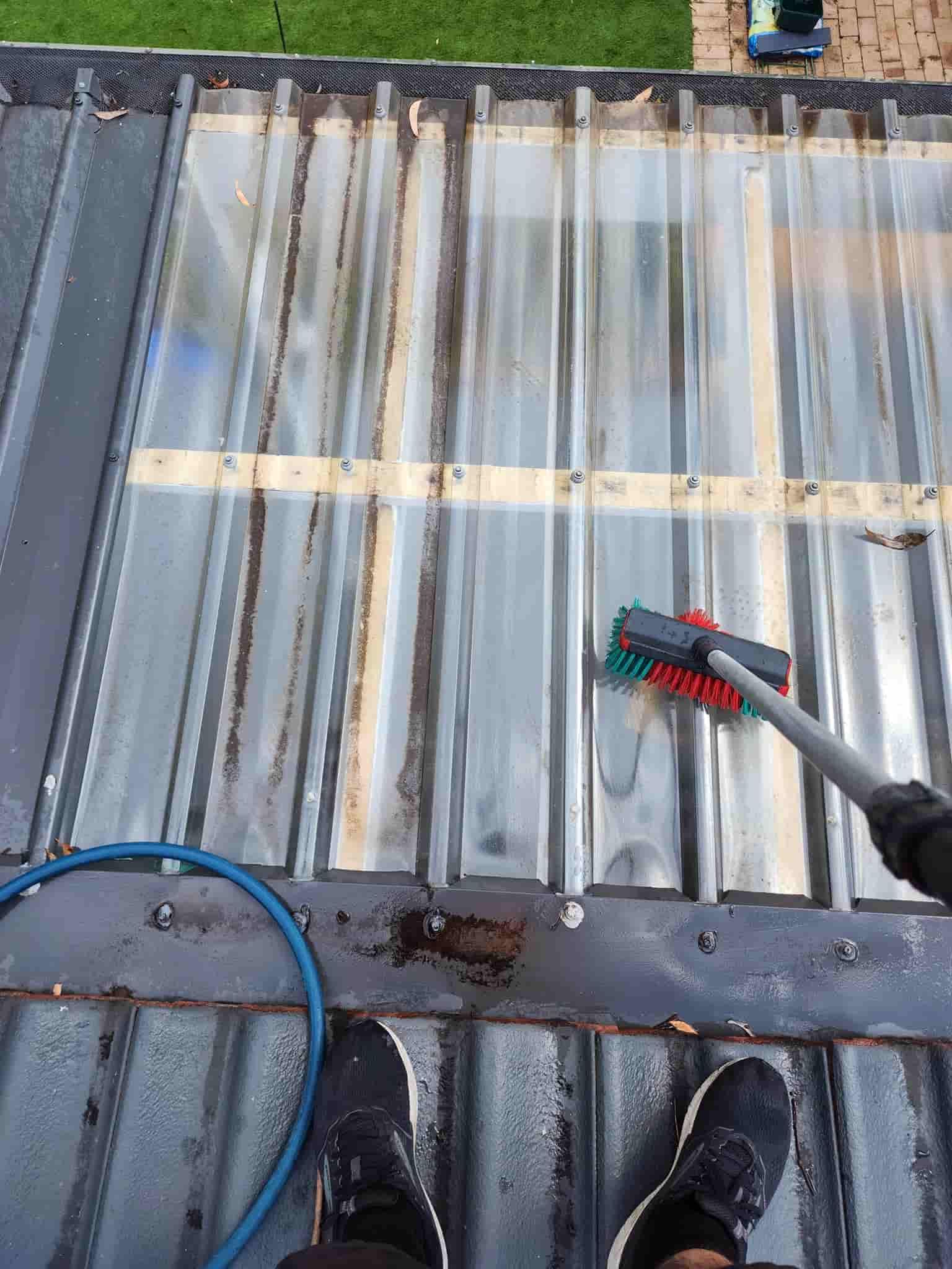 A Person is Cleaning a Metal Roof With a Brush — Exquisite Exterior Cleaning In North Gosford, NSW