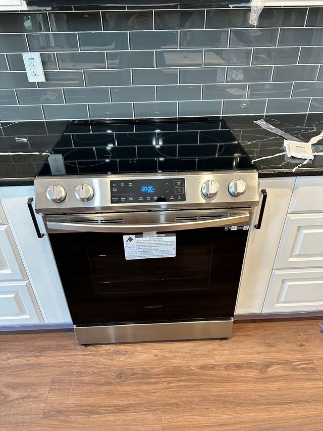 A kitchen with white cabinets, stainless steel appliances, including a range and refrigerator, and wood flooring.