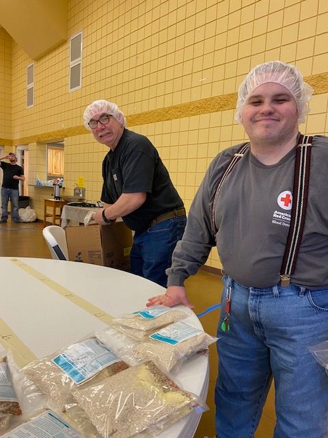 Two men wearing plastic hats are standing next to a table with bags of food on it.
