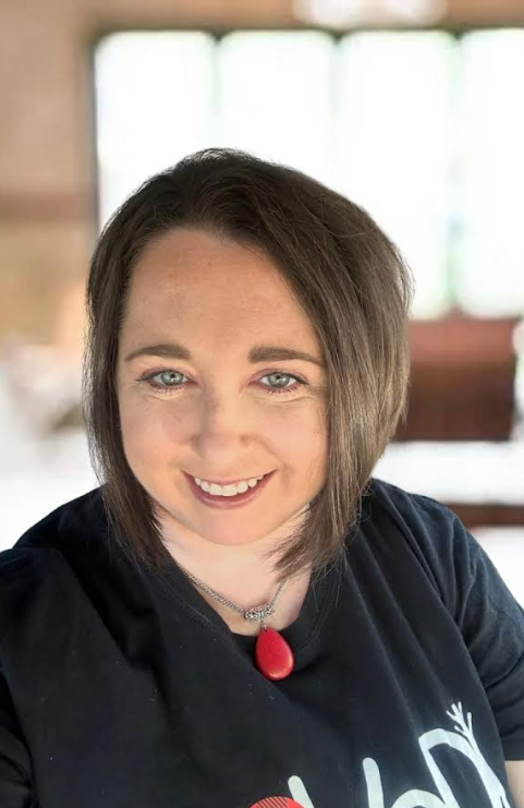 A woman wearing a black shirt and a red necklace is smiling for the camera.