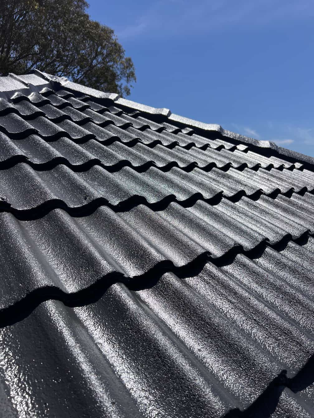 A close-up, high-angle shot of a black tiled roof under a bright blue sky.