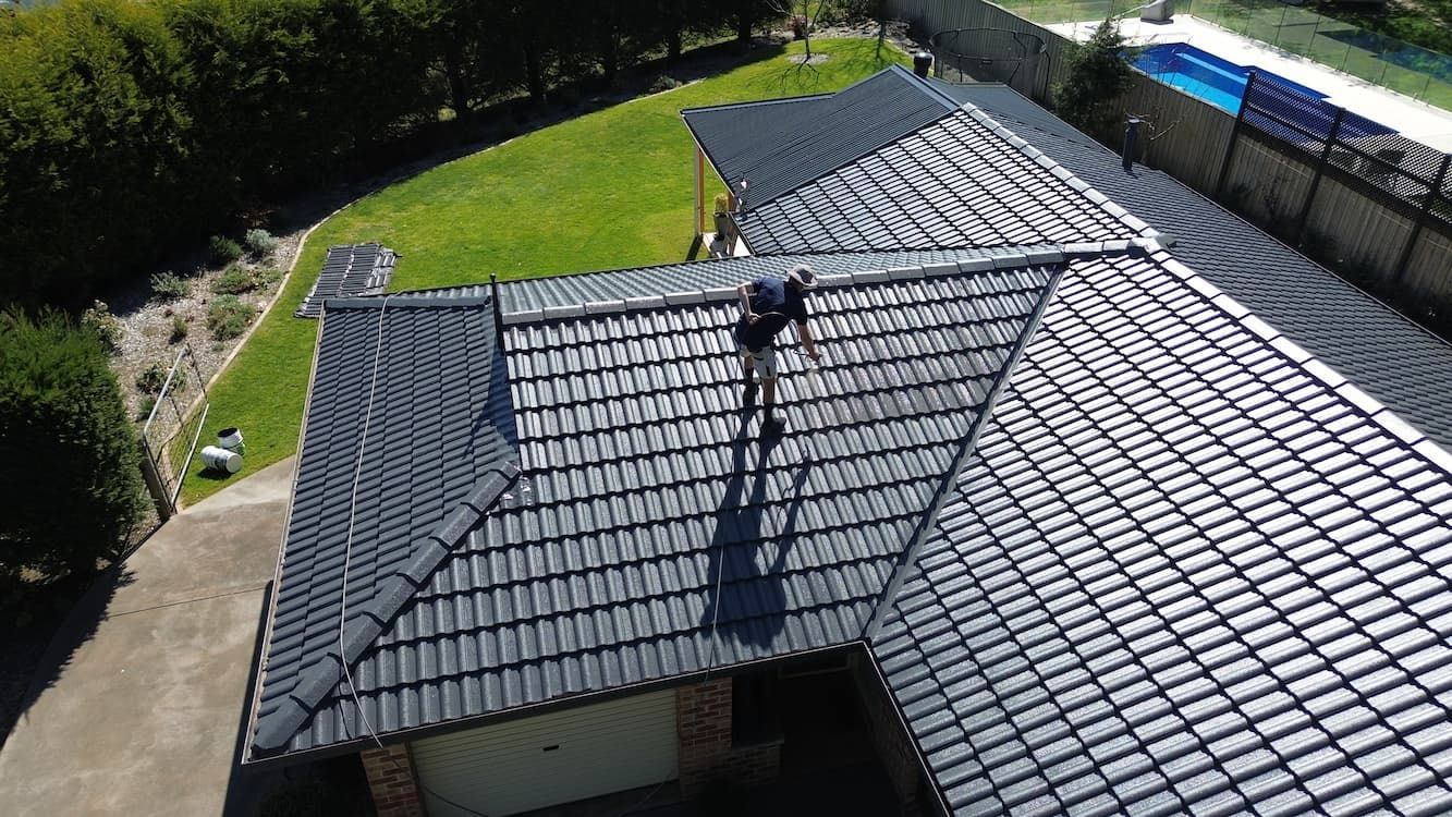 Person on a dark tiled roof, possibly working. Lawn, driveway, and pool are visible in the surrounding area.