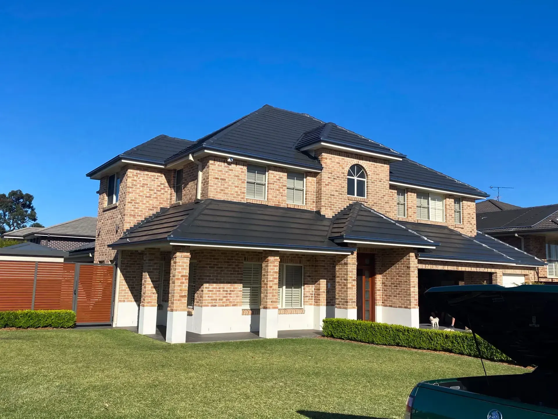 A large brick house with a black roof and a green truck parked in front of it.
