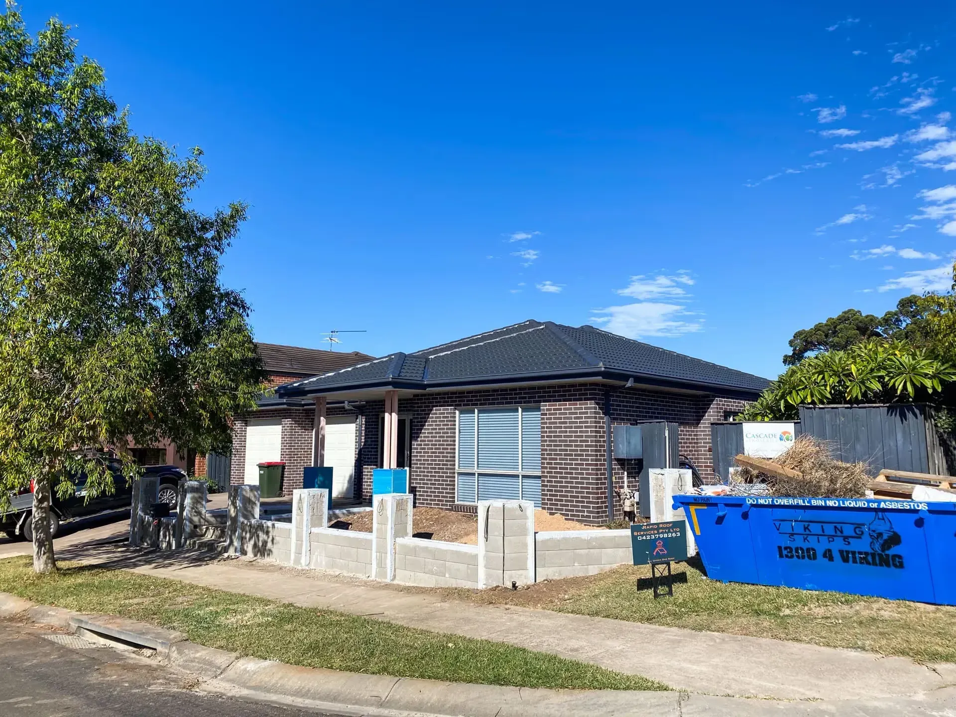 A house under construction with a blue dumpster in front of it.