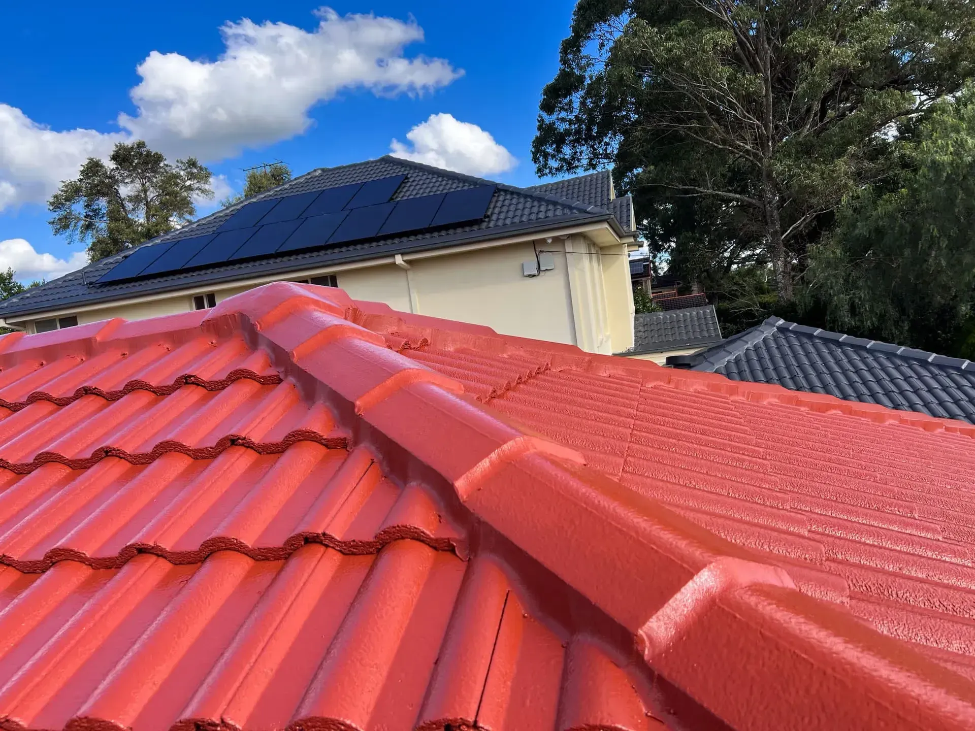 The roof of a house is painted red and has solar panels on it.