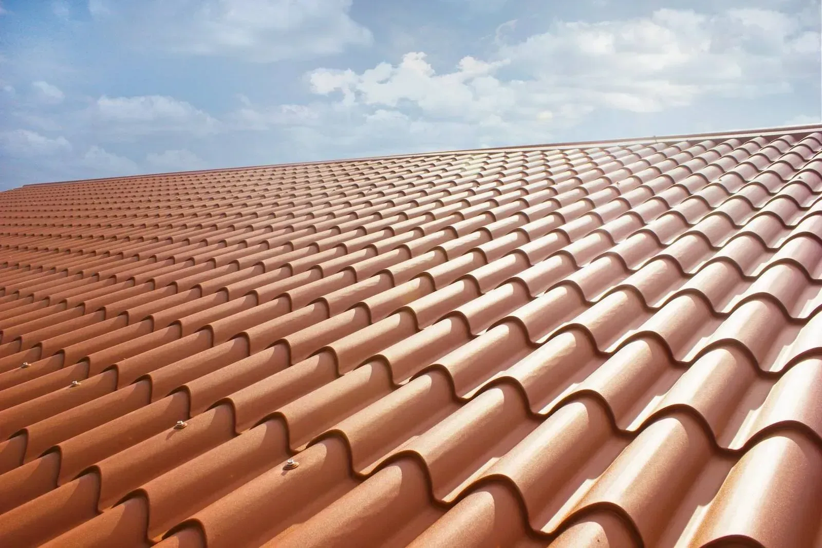 Close-up view of a terracotta tile roof against a blue sky with white clouds.