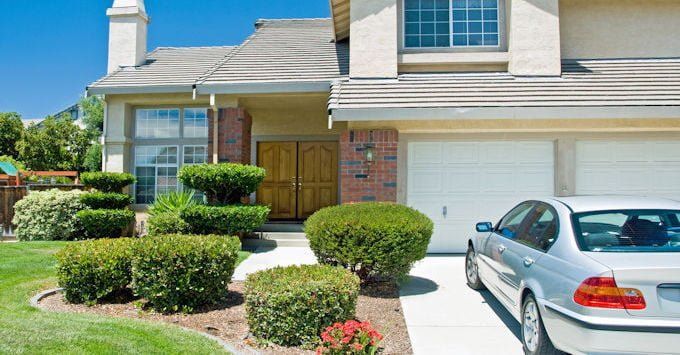 close up of hand holding a white paper umbrella over over white paper cut outs of a family, house, and car covered by insurance