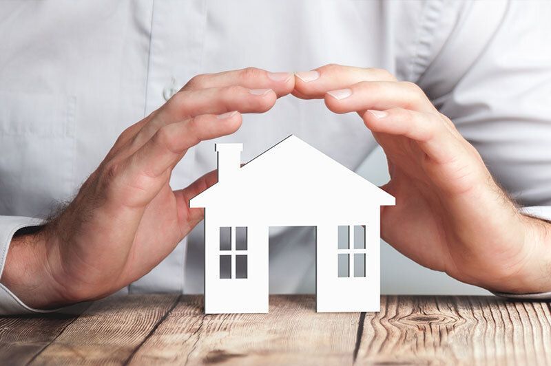 Hands cover small white house model symbolizing home insurance coverage