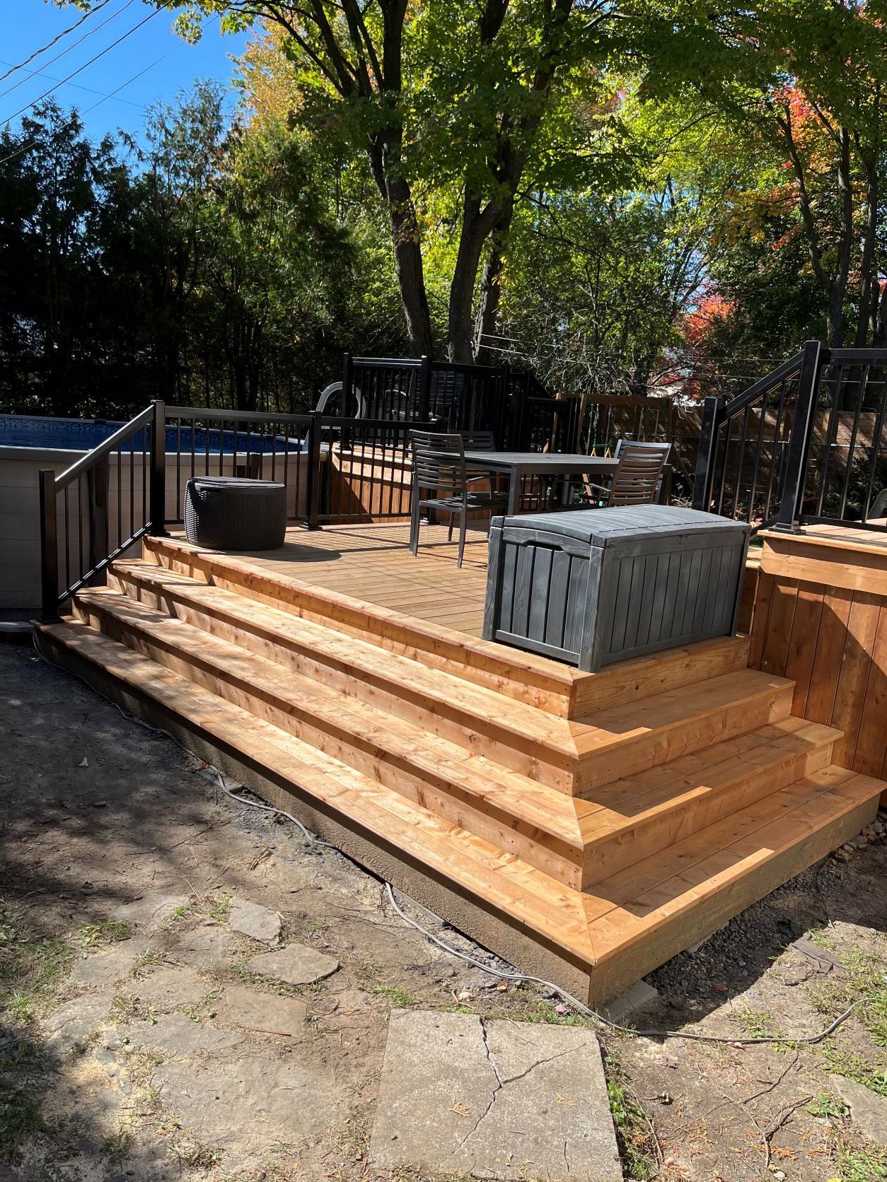 Une terrasse en bois avec des escaliers et une piscine en arrière-plan.