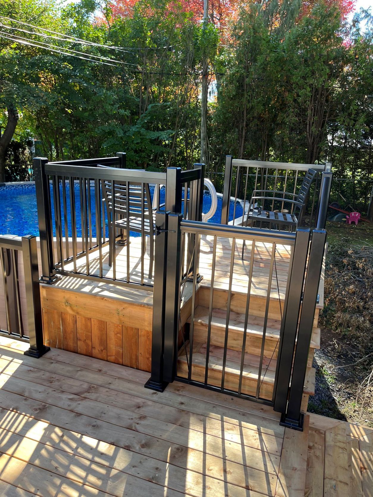 Une terrasse en bois avec un portail en métal menant à une piscine.