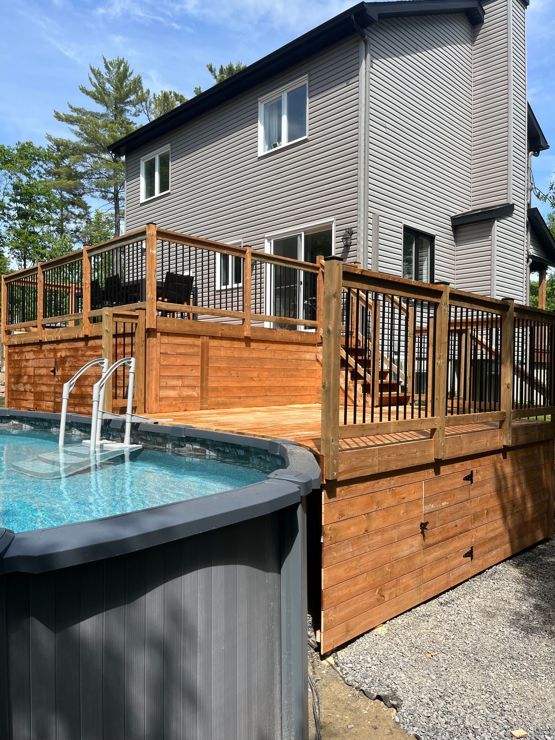 Une piscine est située sur une terrasse en bois à côté d'une maison.