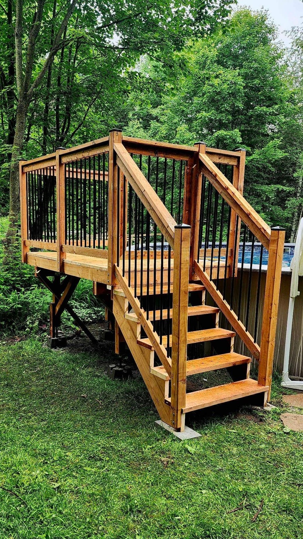 Une terrasse en bois avec des escaliers qui y mènent et un bain à remous en arrière-plan.