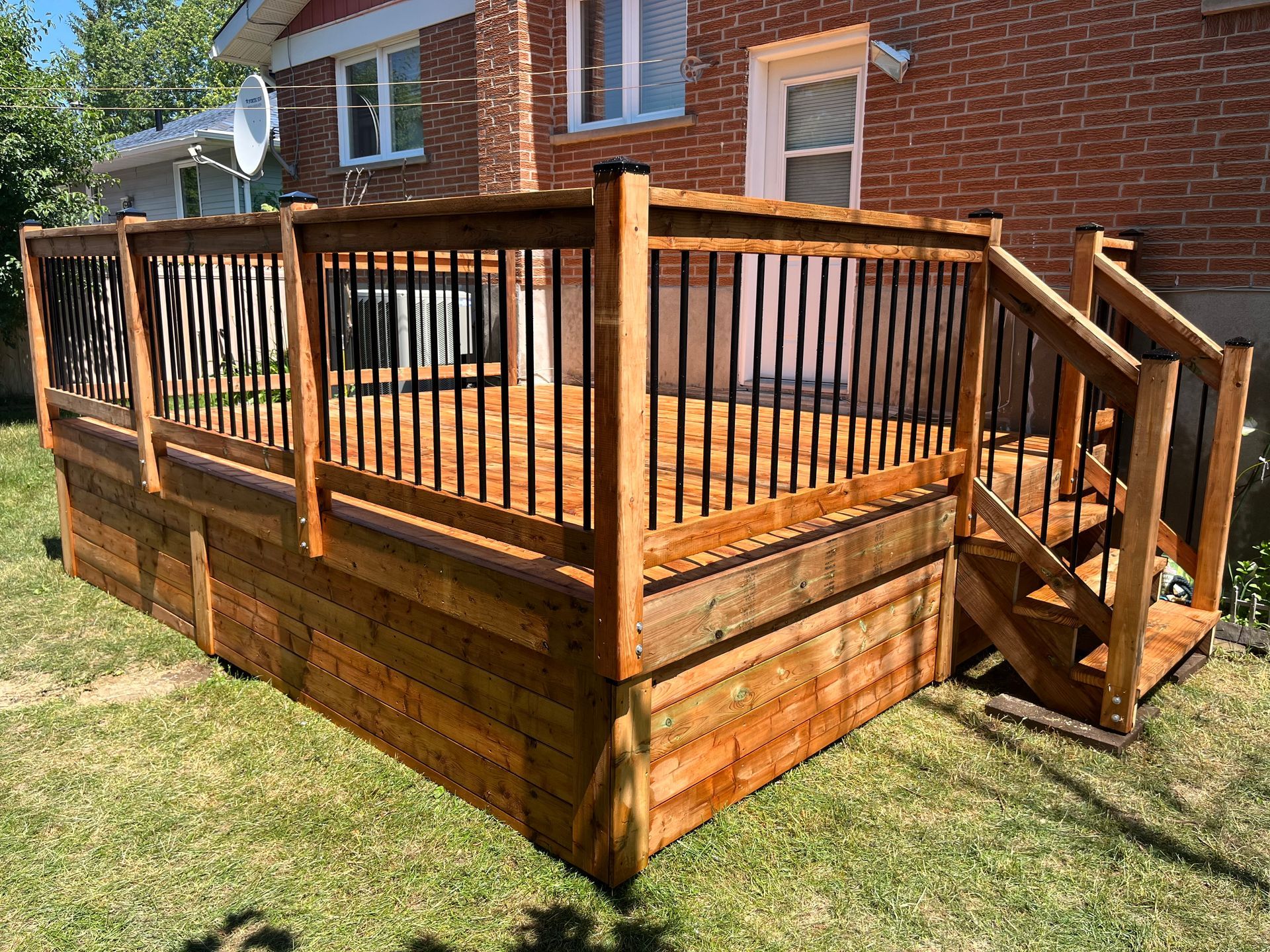 Une terrasse en bois avec escalier et balustrade devant une maison en briques.