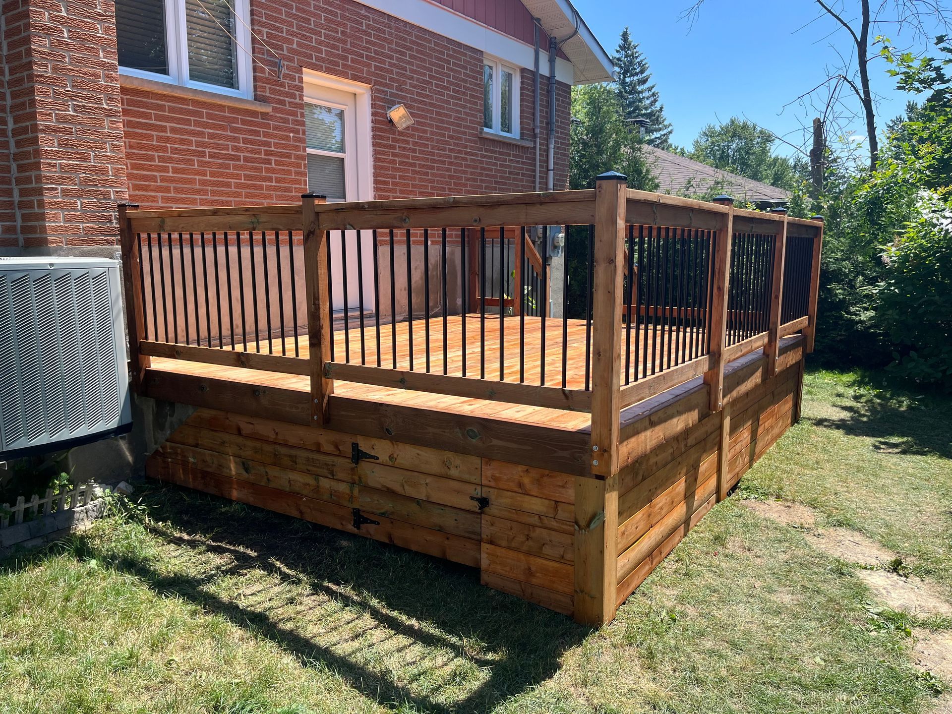 Une terrasse en bois avec une balustrade devant une maison en briques.