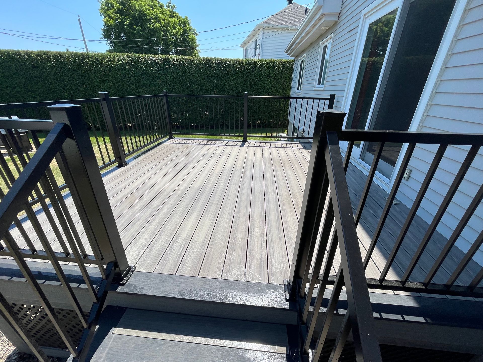 Une terrasse en bois avec une balustrade noire devant une maison.