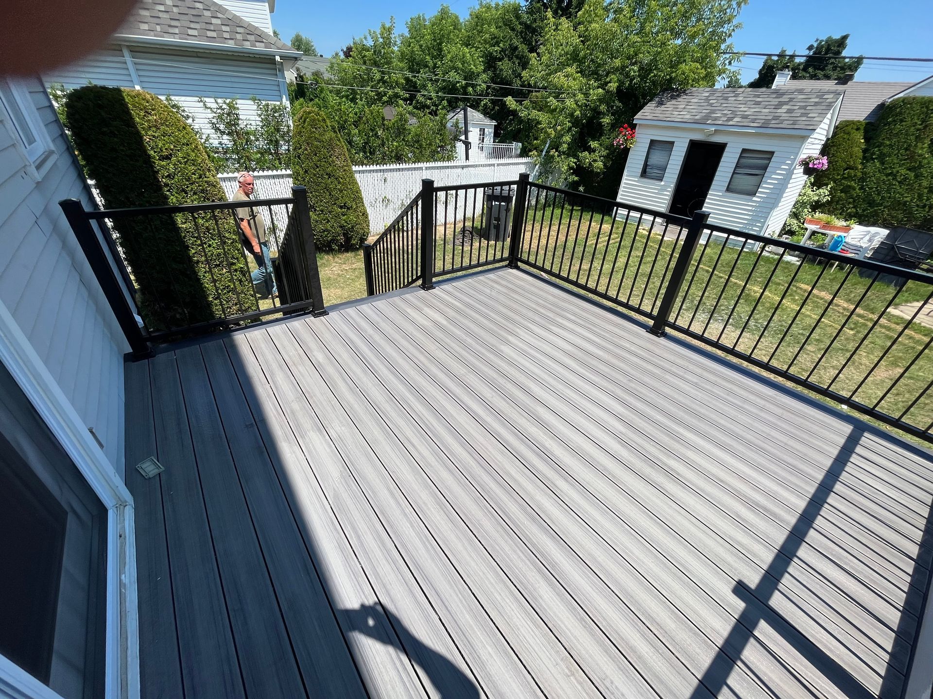 Une terrasse grise avec une balustrade noire et une maison blanche en arrière-plan.