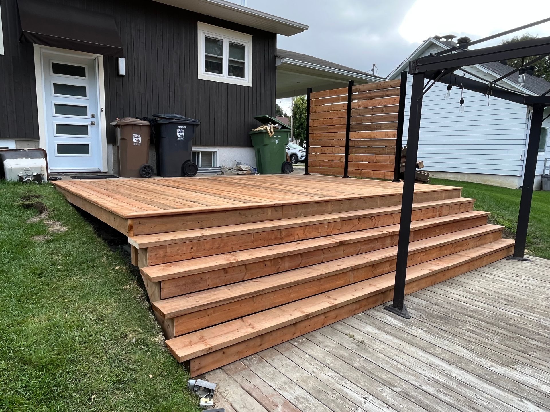 Une terrasse en bois avec des escaliers et une pergola devant une maison.