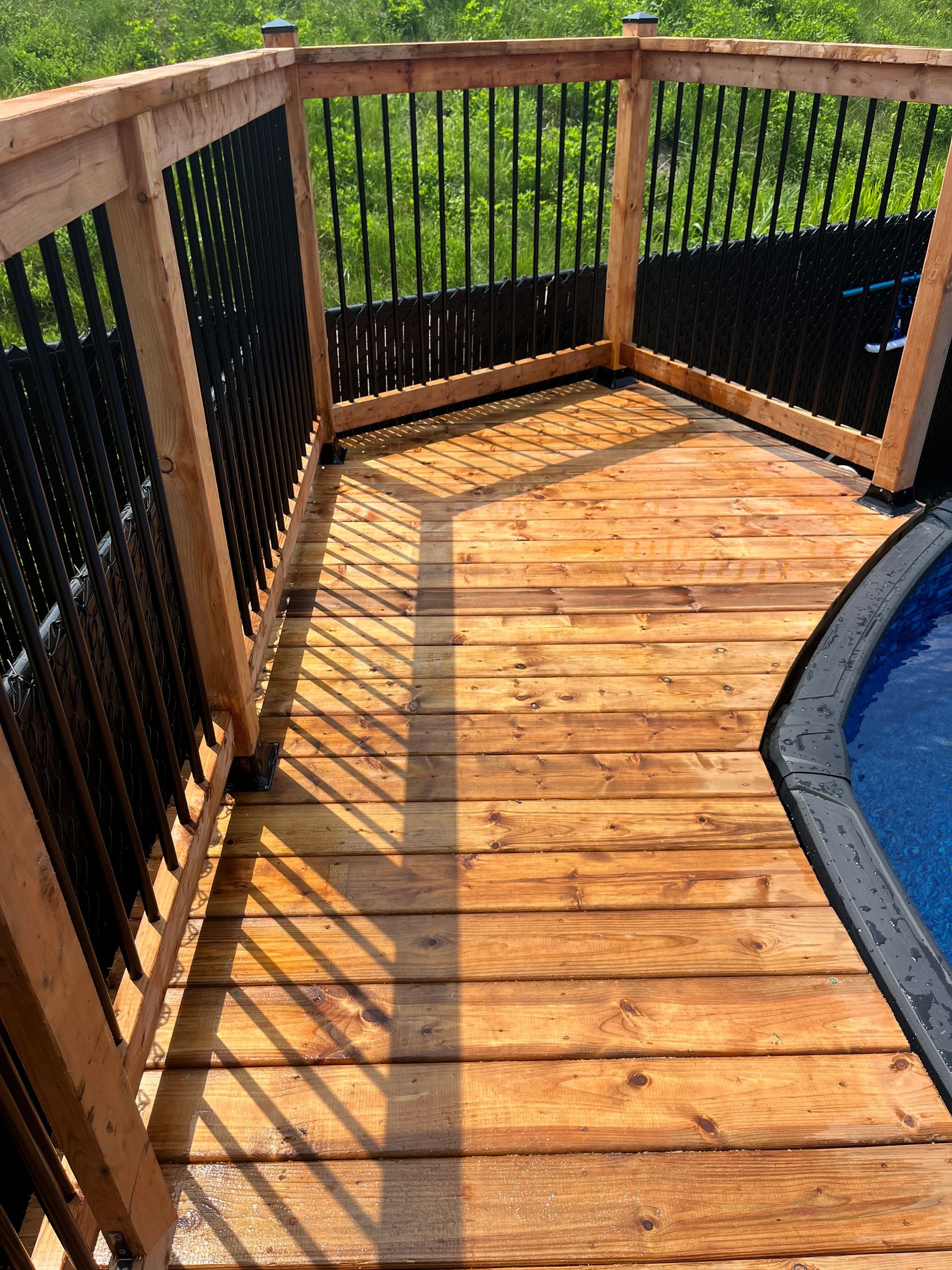 Une terrasse en bois à côté d'une piscine avec une balustrade noire.