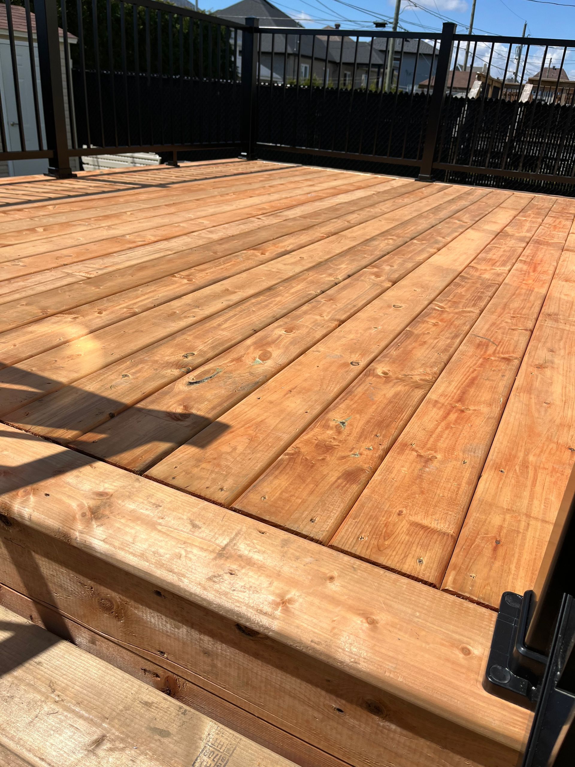 Une terrasse en bois avec des escaliers et une balustrade noire.