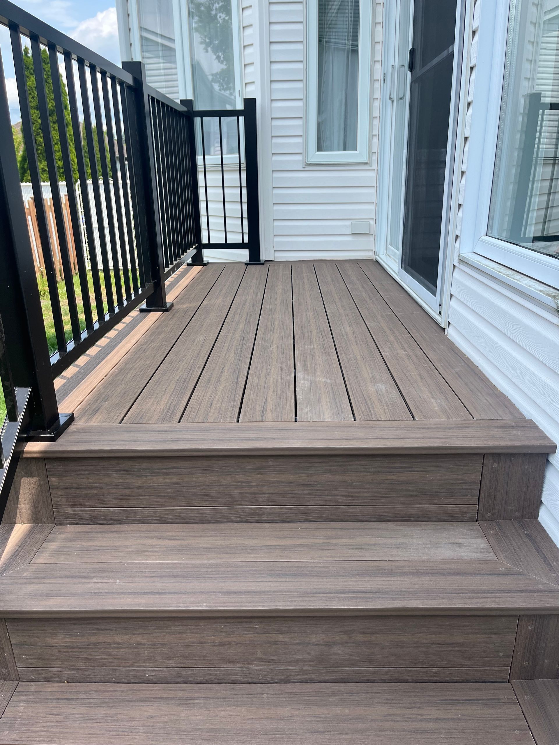 Une terrasse en bois avec des escaliers qui y mènent et une balustrade noire.