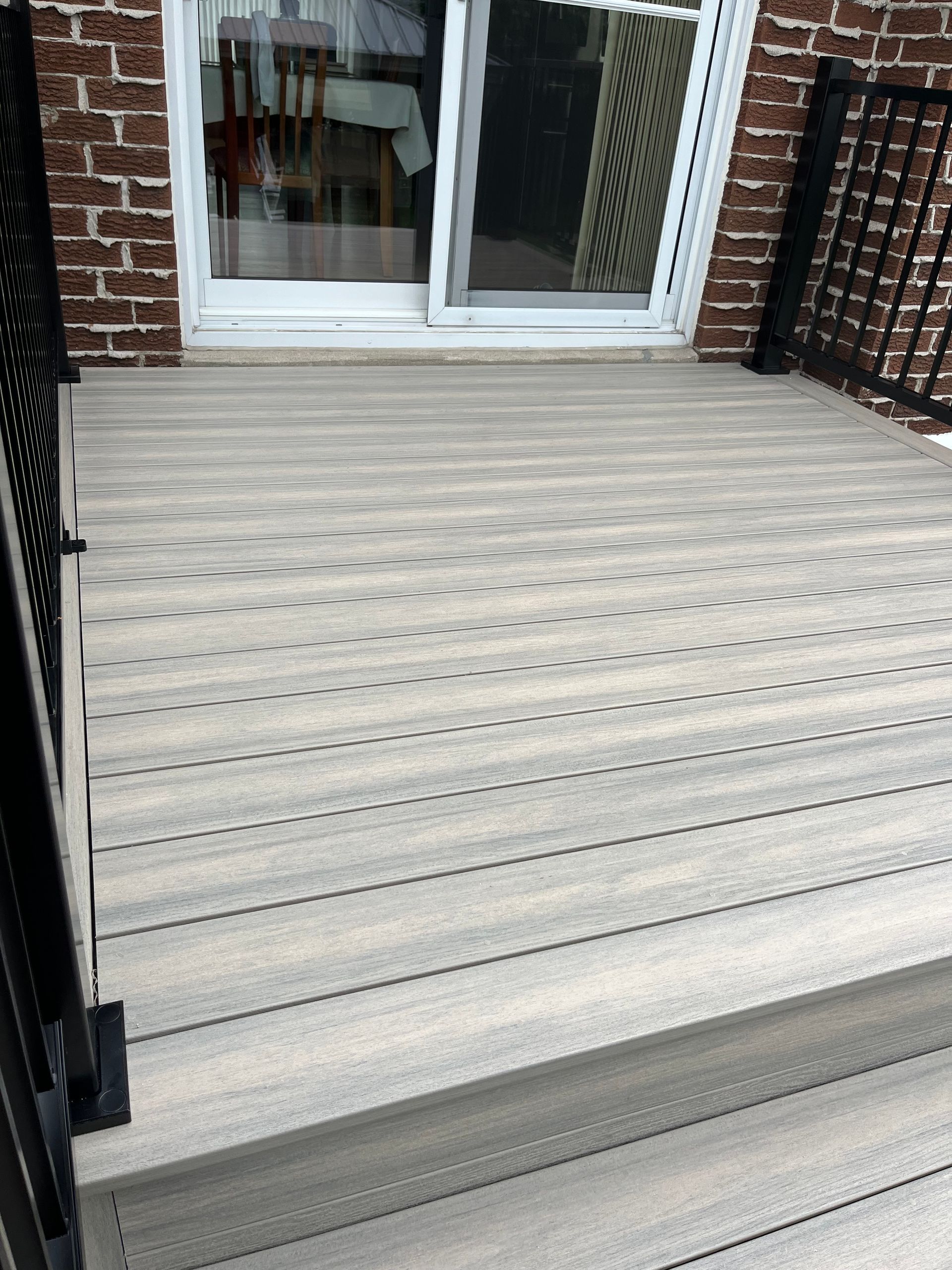 Une terrasse en bois avec des escaliers menant à une porte coulissante en verre.