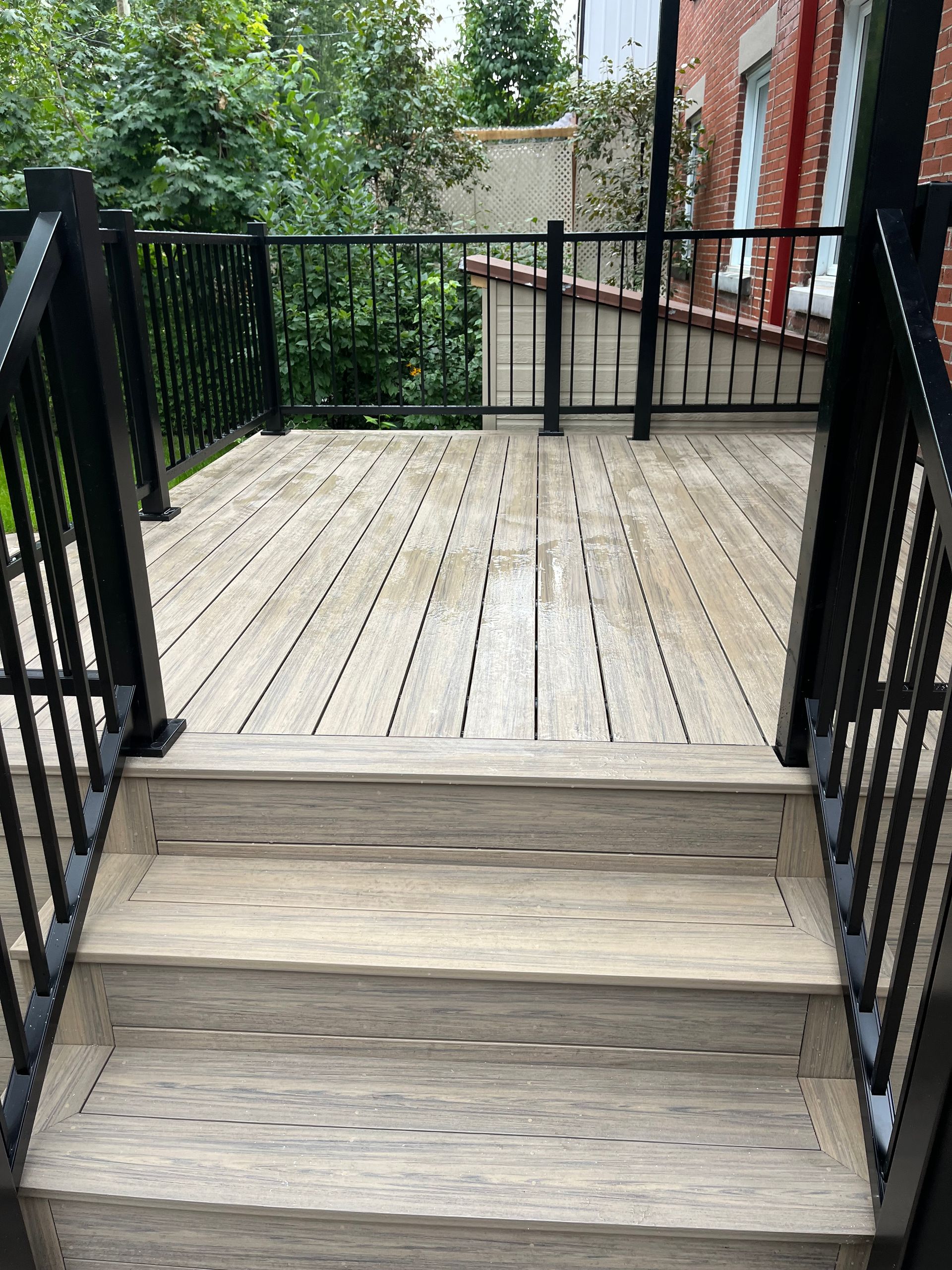 Une terrasse en bois avec des escaliers qui y mènent et une balustrade noire.