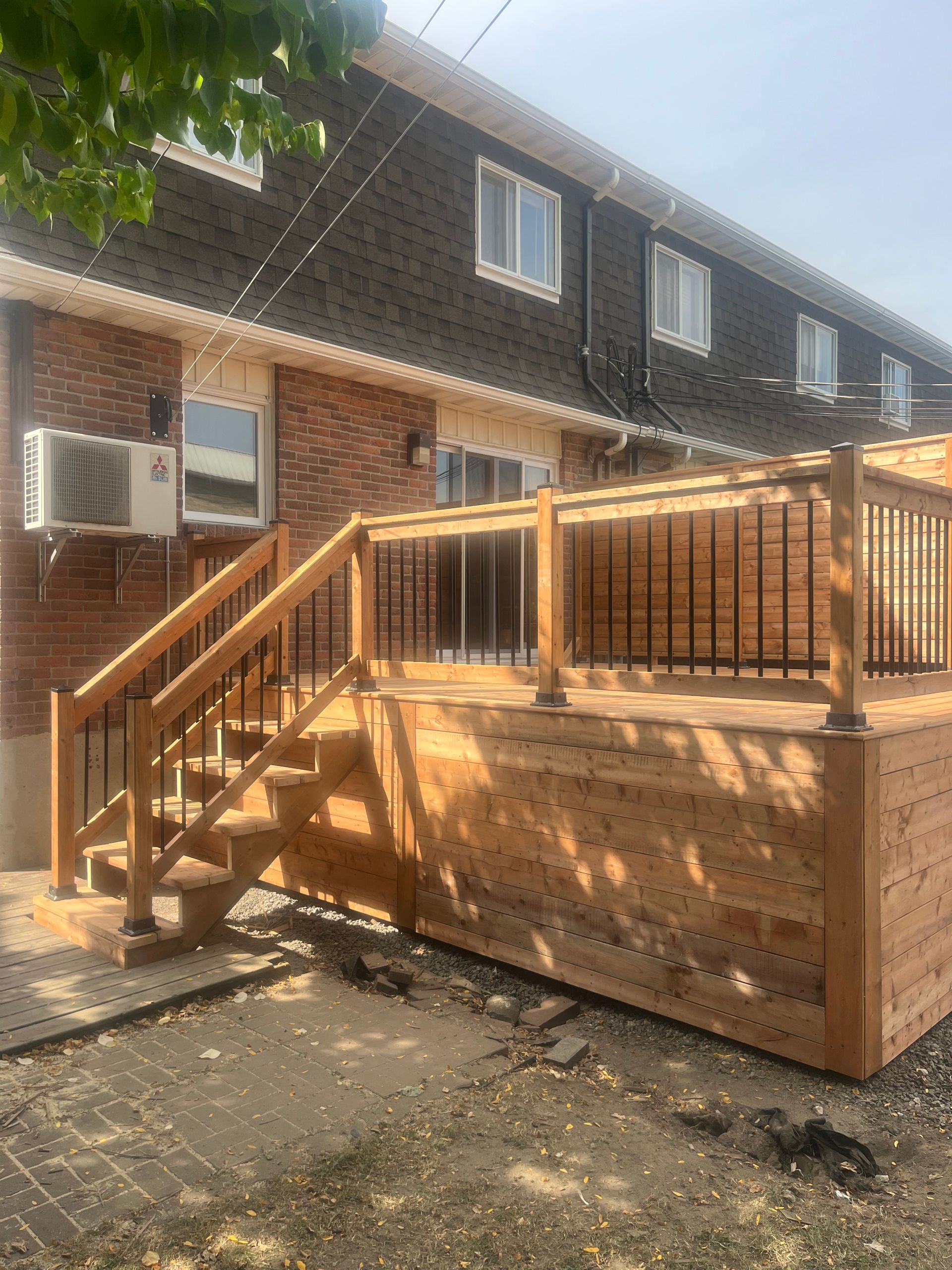 Une terrasse en bois avec des escaliers se trouve devant une maison en briques.