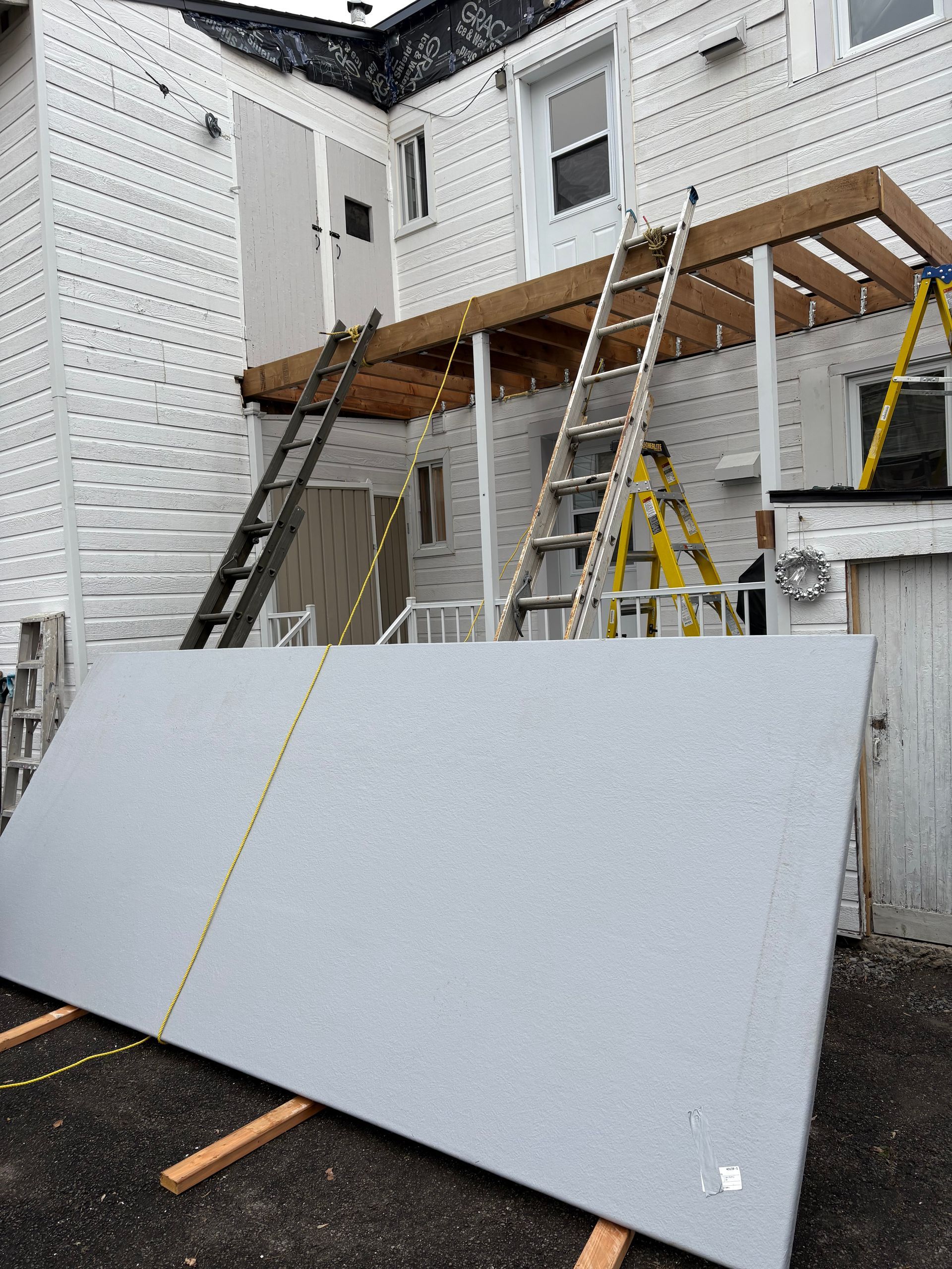 Un grand morceau de carton est posé sur une palette en bois devant une maison.