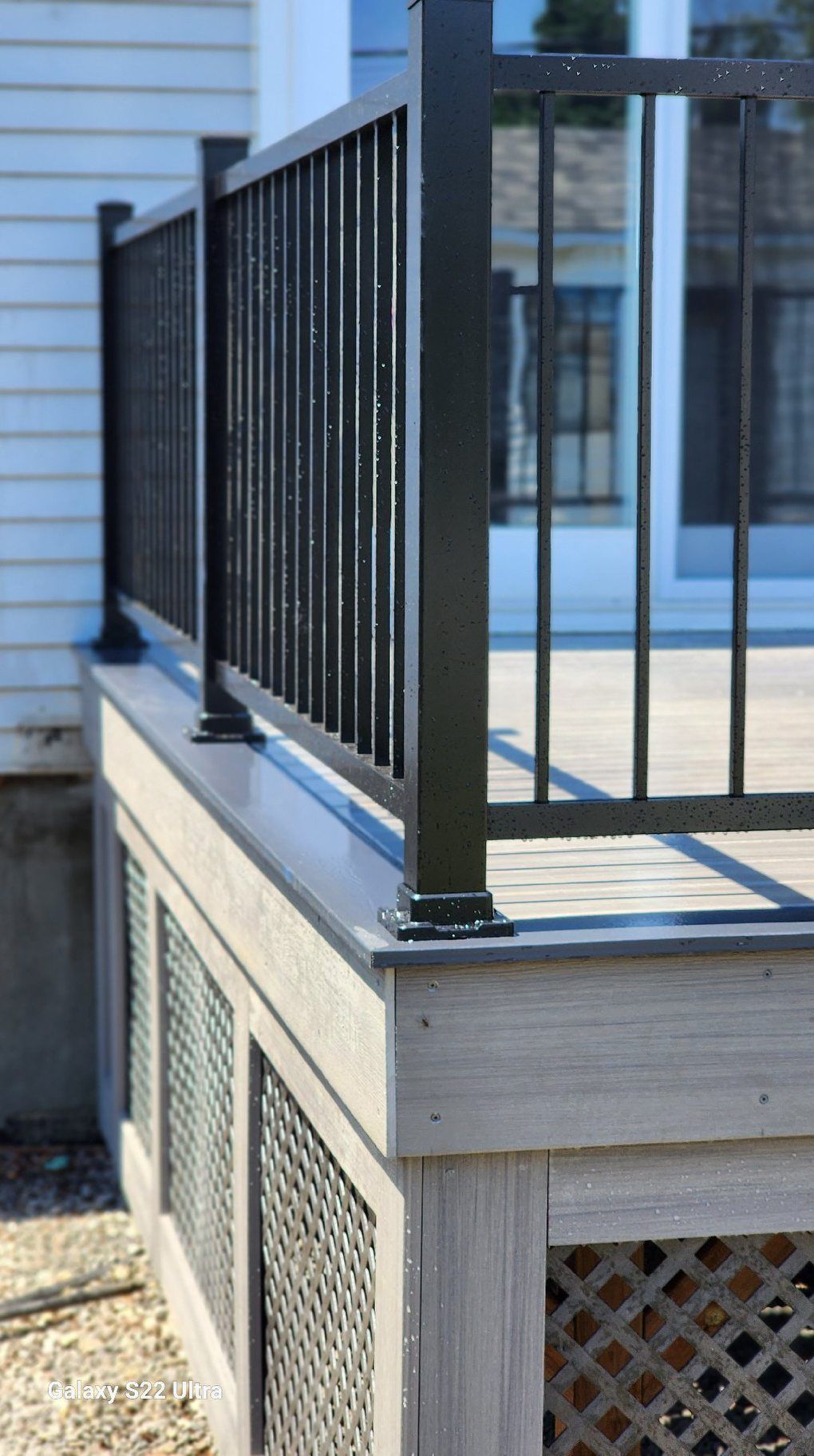 Une terrasse avec une balustrade noire et une maison blanche en arrière-plan.
