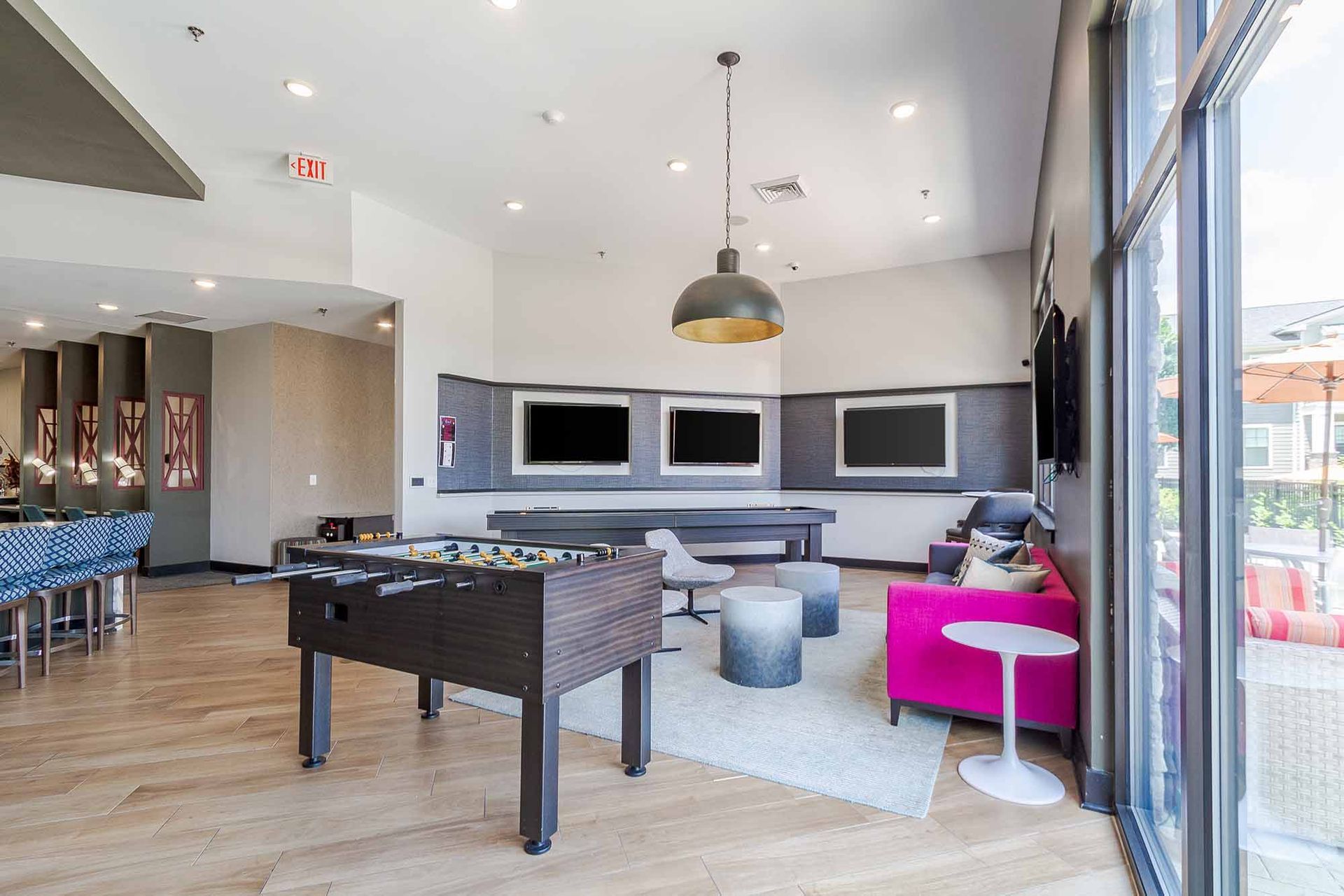 Game room with foosball, three TVs, pink sofa, bar, and outdoor view.